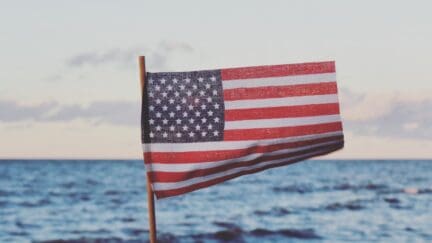 American flag waving over the ocean, symbolizing holiday weekend for real estate home sales.