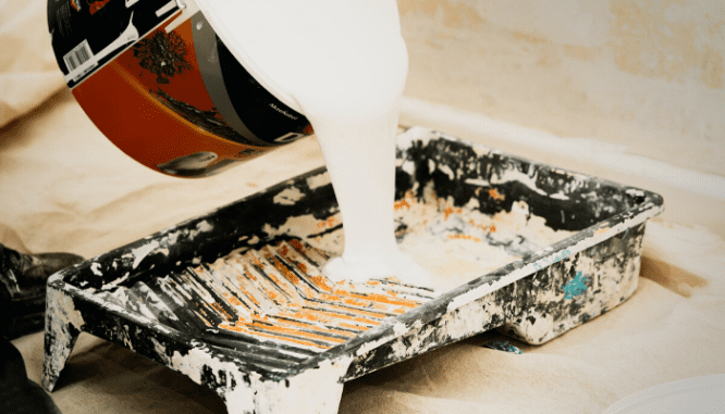 A close-up of paint being poured into a tray which could be used for home maintenance.