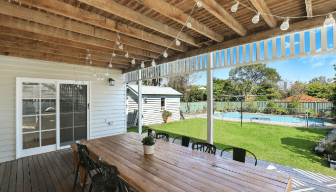 A dining table on a back porch with string lights and a pool in the background, which may be home resale value factors.