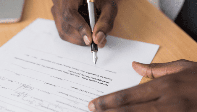 Hands signing a mortgage which may involve a mortgage overlay.