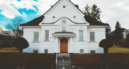 A grand white house with hedges and two stories.