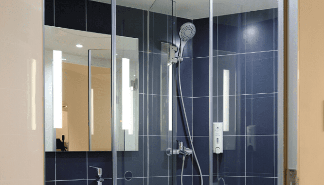 A glass shower stall in a blue tiled bathroom, a home improvement to a small house.