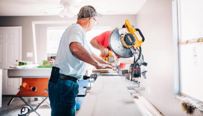 A man using a table saw in a white room.