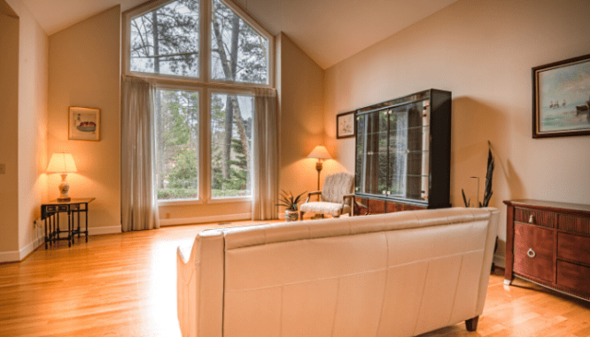 A living room with a display cabinet, a tan couch, and giant loft windows.