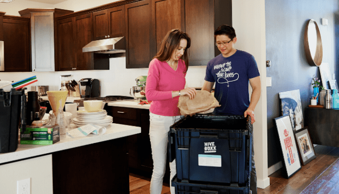 Two people packing things from a kitchen into a reusable box for moving.
