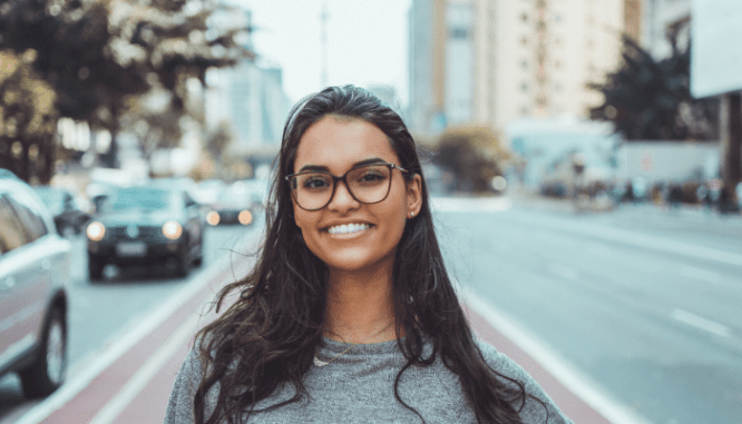 A woman with long brown hair and glasses is smiling.