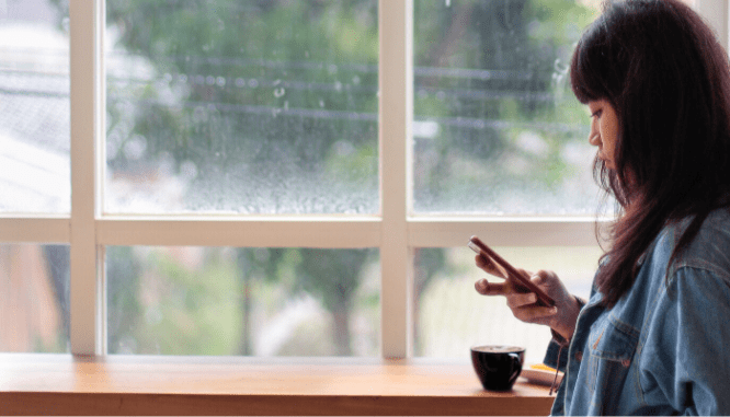 A woman looking at her phone screen in a coffee shop, trying to get more house showings.
