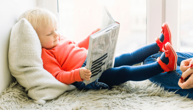 A toddler lying on a pillow and reading a book, getting settled into your new home.