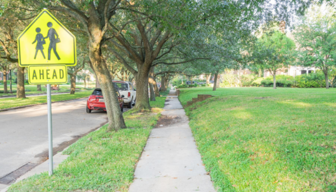 A summery view of a sidewalk near a school crossing sign, a school district which could have an impact on your property values.