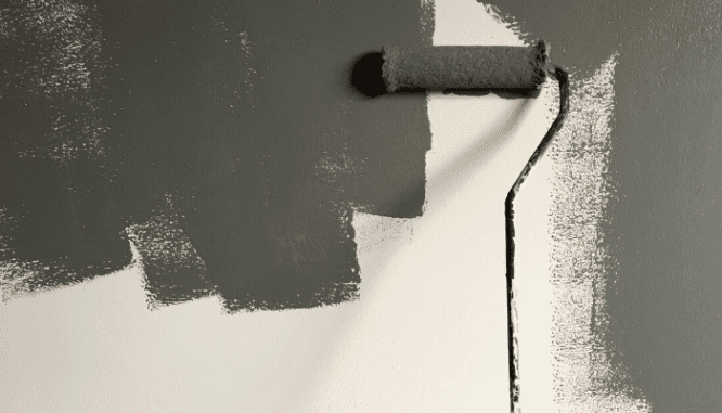 Someone using a paint roller to paint a white wall gray after moving into a new house.