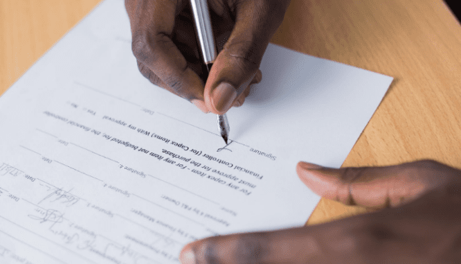 A black man's hands signing an under contract document.