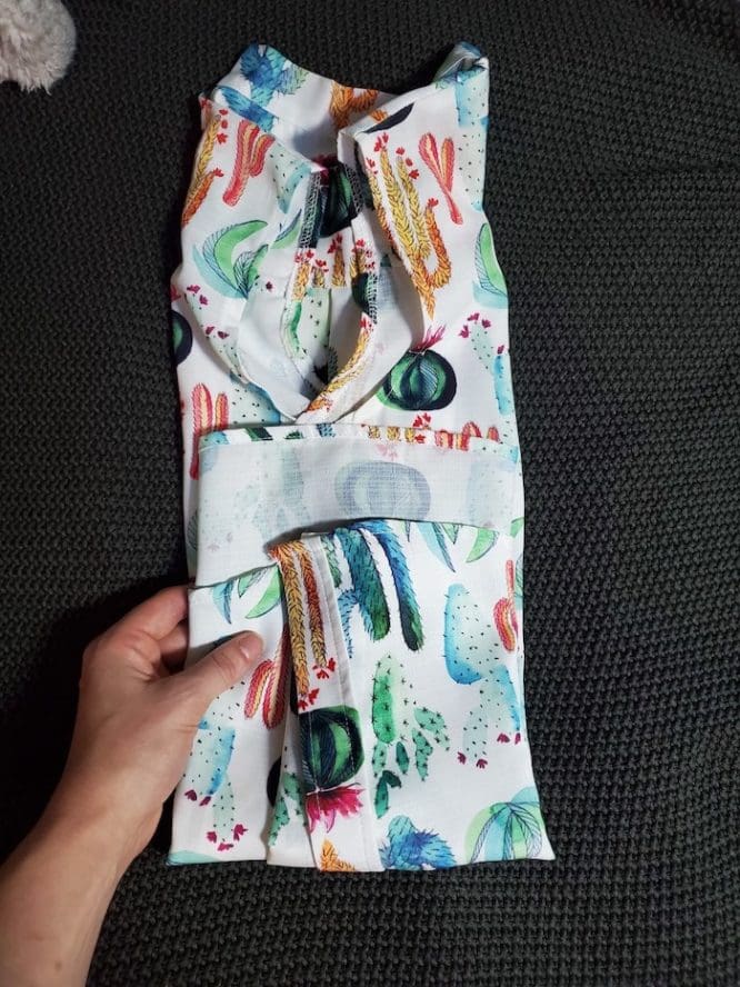 A shirt with a cactus print getting folded into thirds from bottom hem to collar for a flat-fold step to show how to pack clothes for moving