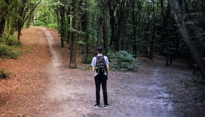 A young man standing at a crossroads in the woods to suggest a hard question he's asking himself about mortgage rates