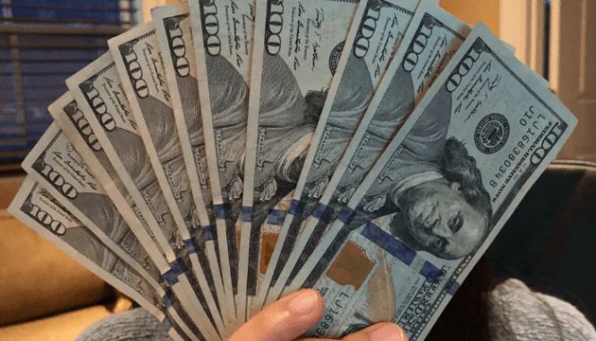 A woman holds a fan of one hundred dollar bills after learning what happens when you sell a house for a profit.