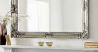 A decorative mirror rests above a fireplace mantel, which is a popular way to decorate with mirrors.