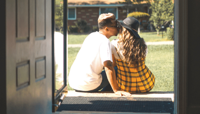 a couple sitting in the doorway of their home, deciding whether to pay it off or invest.