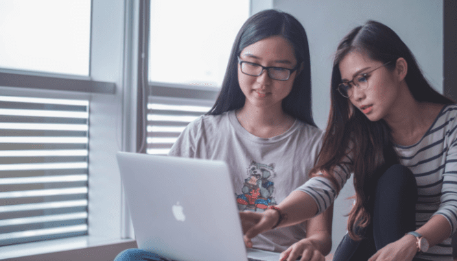 Two girls look over a laptop screen with questions to ask a mortgage broker.