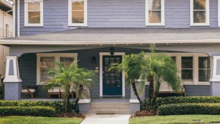 A violet craftsman-style house in Tampa with a dark blue, paned-glass front door, and small palm trees framing the entrance to the house.