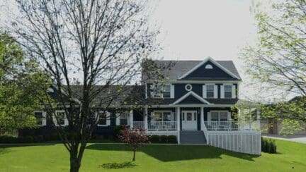 Navy blue farmhouse with white trim and a large grassy front yard. The leaves on the trees in the yard are just starting to sprout.