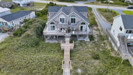 Drone shot of a gray, multi-story beach house on Topsail Beach in North Carolina. There is a wooden boardwalk that extends from the house to the sandy beach.